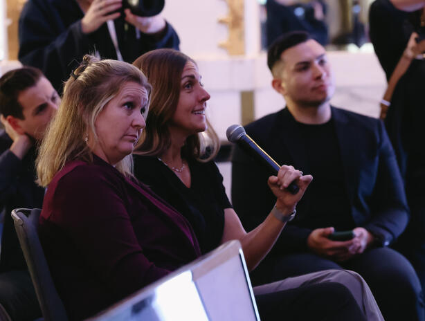 Amber sitting in an audience holding a mic, looking toward stage.