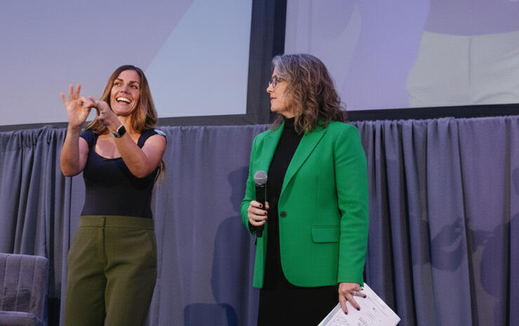 interpreter on stage next to a hearing presenter, signing the word connect.